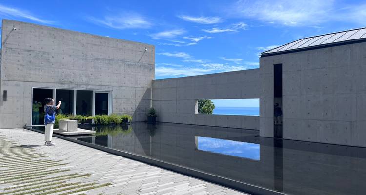 Edificio de hormigón minimalista moderno con piscina de reflejo y un visitante tomando una foto.