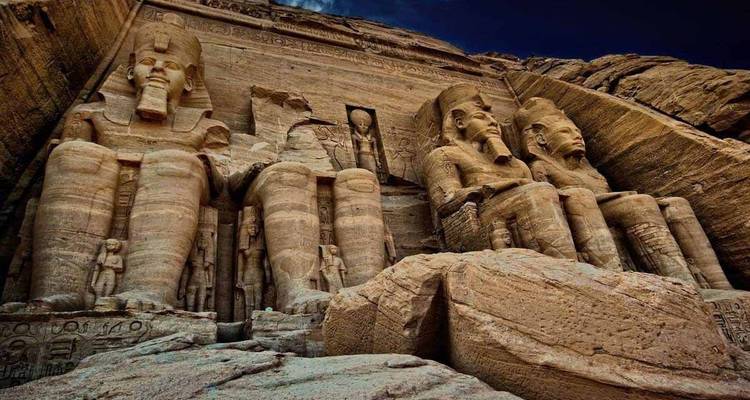 Large ancient statues carved into a cliff, likely Abu Simbel.