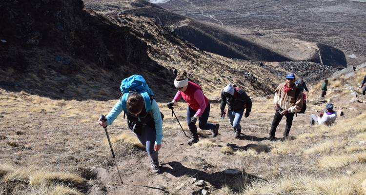 Hikers ascending a steep sandy path in a mountainous area.