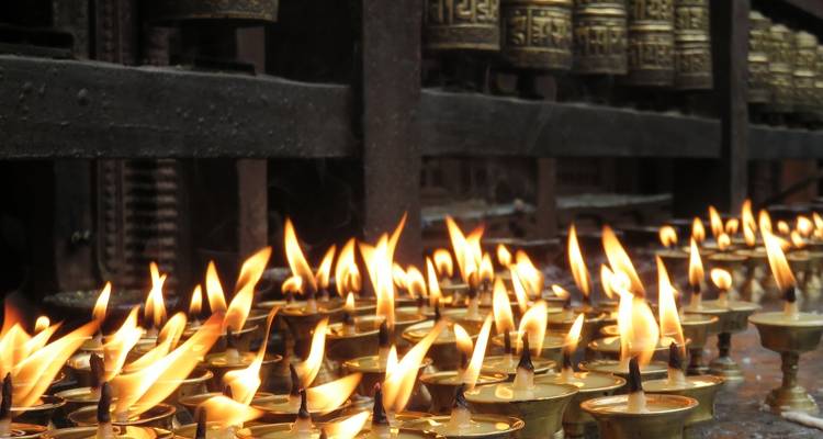 Reihen brennender Votivkerzen vor Gebetsmühlen.
