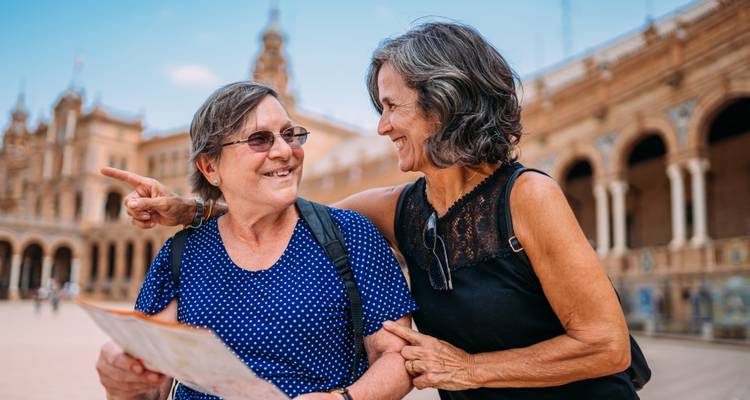 Two older women happily reading a map at an ornate plaza with Moorish arches.