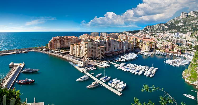 Stunning aerial view of Monaco harbour filled with yachts, backed by sea and steep hills.