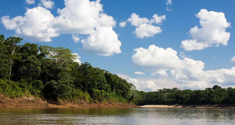 River winding through dense forest under a blue sky with white clouds.