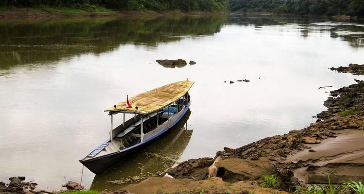 A small boat moored on the riverbank under a cloudy sky.