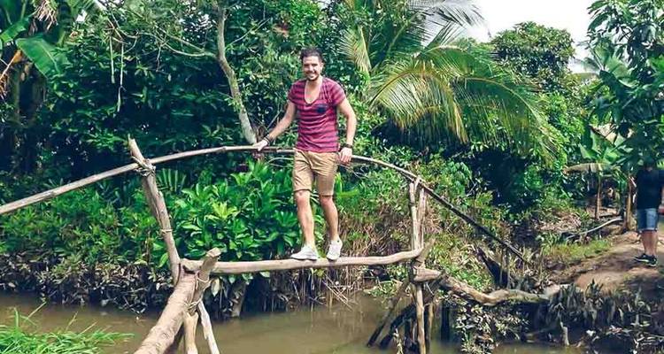 Persoon die een bamboebrug oversteekt in weelderig terrein.