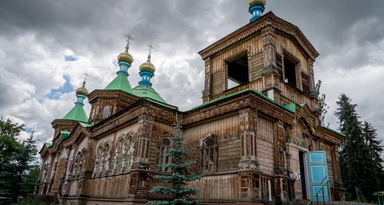 Iglesia ortodoxa de madera desgastada con techos verdes y detalles azules bajo unas nubes impresionantes.