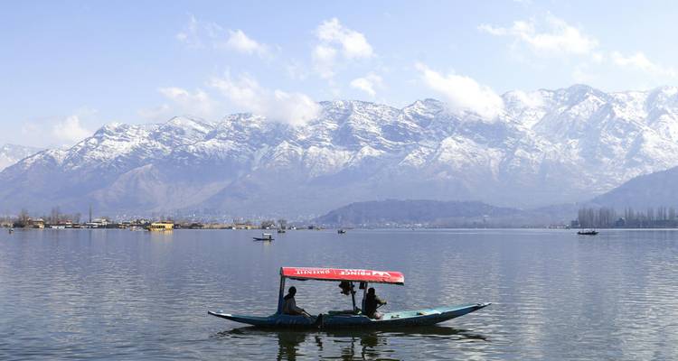 Un bateau shikara avec deux passagers flotte sur le lac Dal sur fond de pics enneigés.