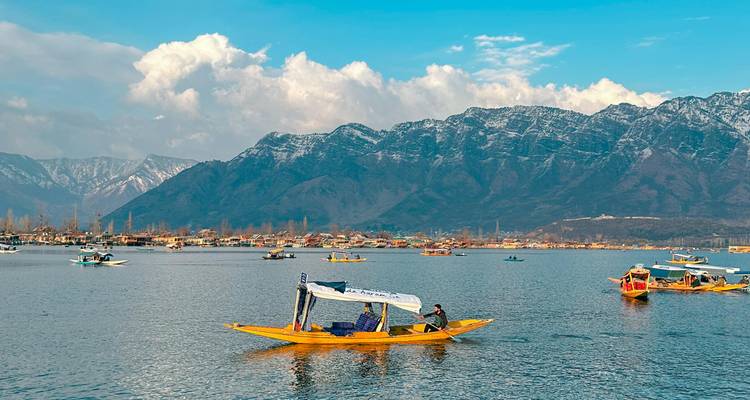 Des shikaras colorés parsèment le lac Dal avec des montagnes enneigées et un ciel bleu au loin.