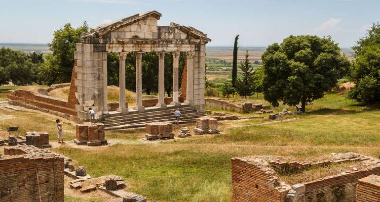 Antiguas columnas de mármol y plataforma de templo en ruinas ubicadas in un parque arqueológico con césped donde los visitantes exploran.