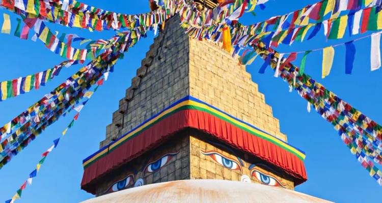 White stupa crowned with Buddha eyes and vibrant prayer flags fluttering against a clear blue Nepalese sky.