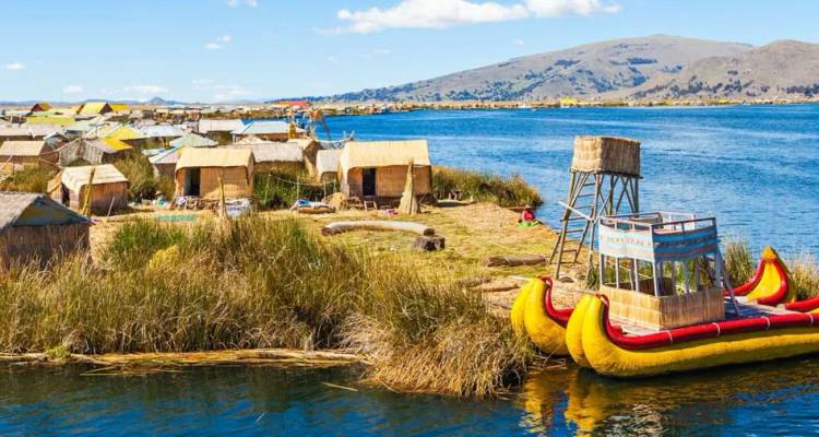 Traditional reed houses and bright yellow reed boat on the floating islands of Lake Titicaca.