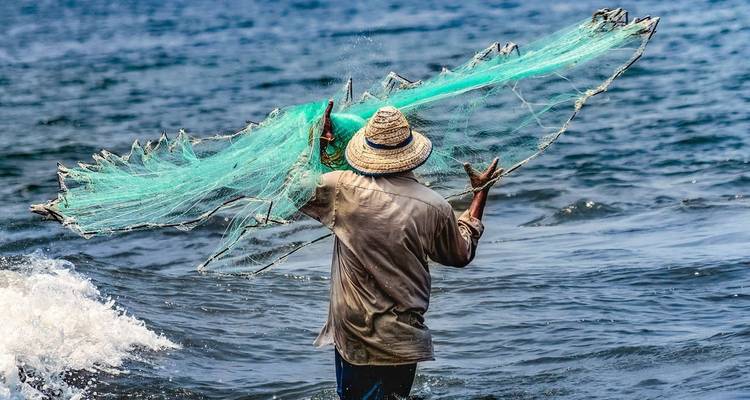 A fisherman casting a net into the ocean from the shore.