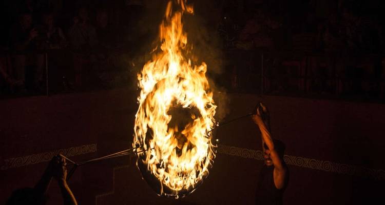 A performer holding a flaming ring in a dimly lit space.