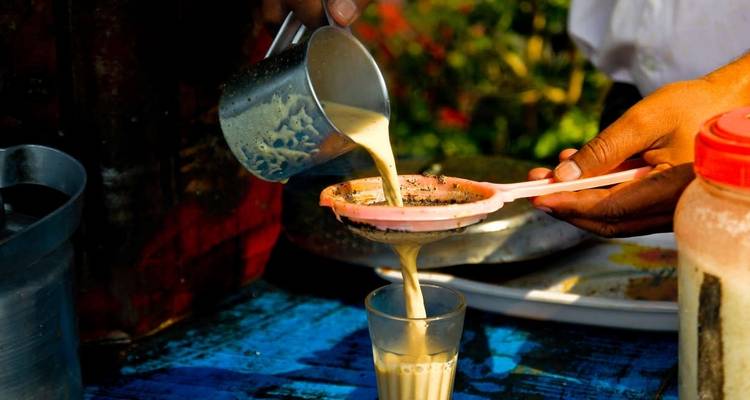 A person pouring a traditional beverage through a strainer into a glass.