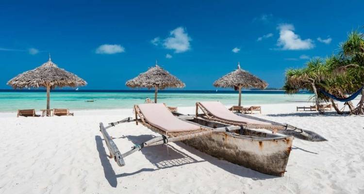 Ein sandiger Strand mit hölzernen Liegestühlen und Strohsonnenschirmen.