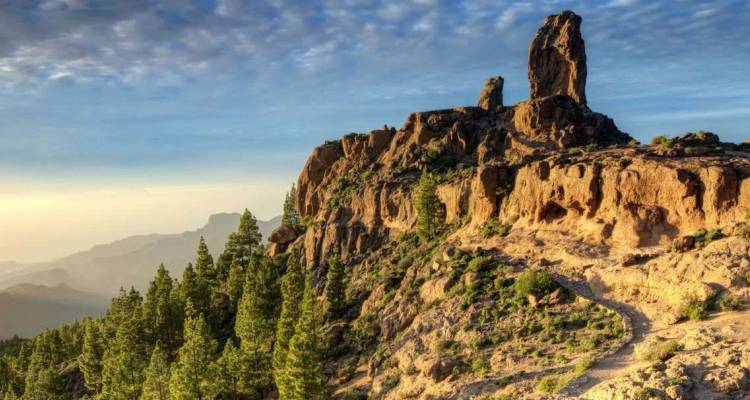 Pic rocheux de Roque Nublo s'élevant au-dessus des forêts de pins et des sentiers poussiéreux de Gran Canaria au coucher du soleil.