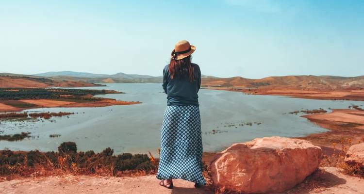 Frau, die über eine große Wasserfläche blickt, umgeben von einer ländlichen Landschaft.