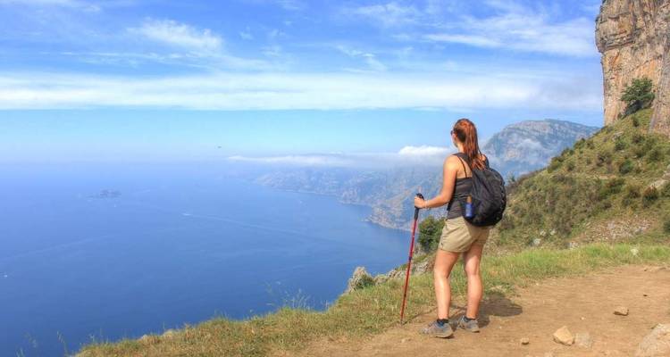 Frau wandert mit einem Wanderstock und blickt auf eine Küstenlandschaft.