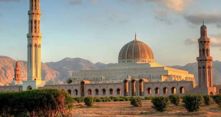 Grote Sultan Qaboos Moskee met hoge minaretten en bergen op de achtergrond in warm avondlicht