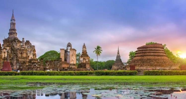 Ancient brick stupas and temple spires reflected in lotus pond at sunrise in Sukhothai.