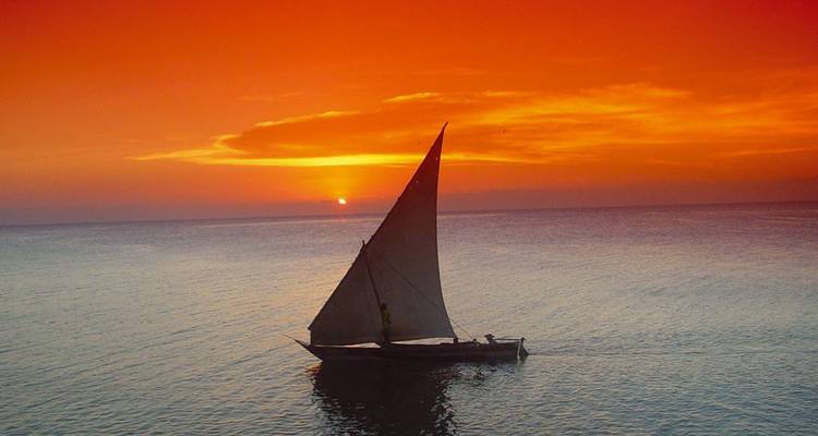 Traditional dhow sails across calm Indian Ocean waters during a vivid orange sunset.