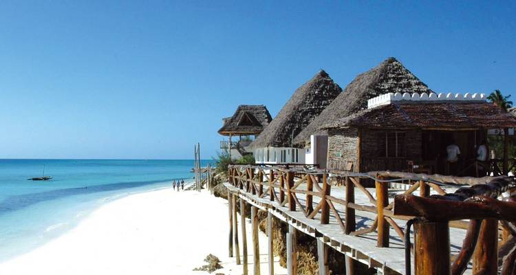 White sand beach with turquoise water and thatched seaside bungalows on wooden stilts.