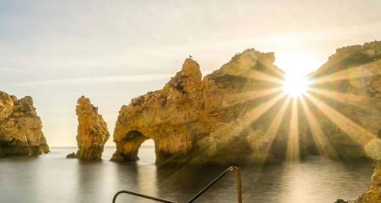Goldenes Sonnenlicht bricht durch dramatische Kalkstein-Meeresbögen, die aus ruhigen Küstengewässern aufragen.