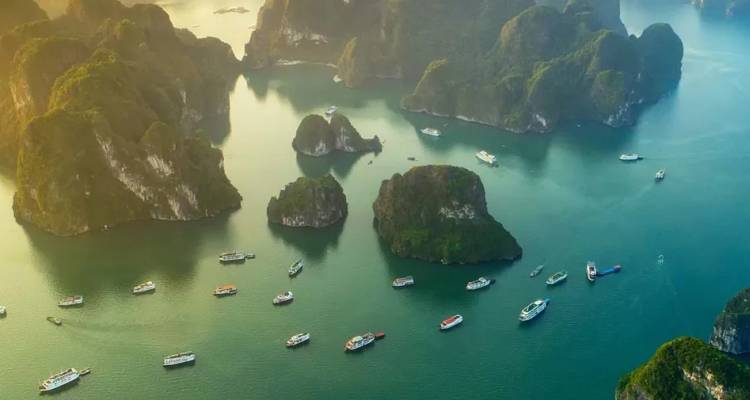 Luchtfoto van smaragdgroene wateren vol met kalksteeneilandjes en cruiseschepen in de rustige lagune van Halong Bay.