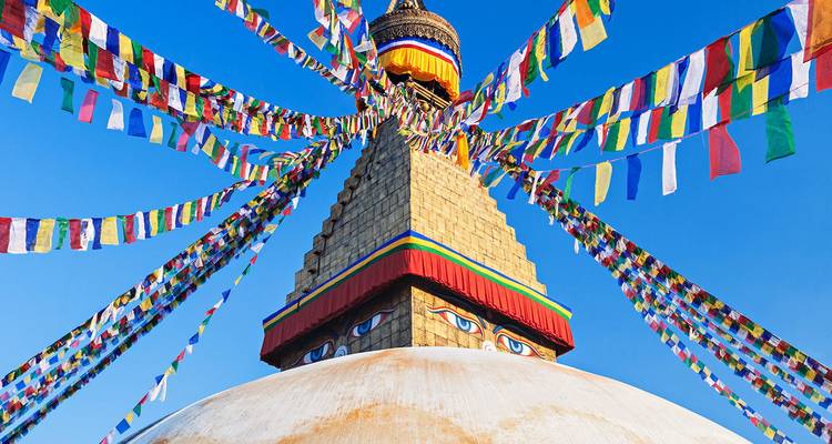 Golden Boudhanath Stupa capped with the all-seeing eyes, radiating colorful prayer flags against a deep blue sky.