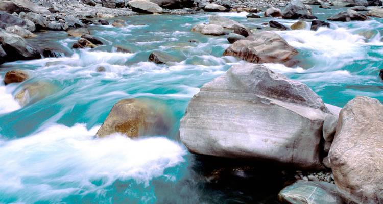 Silky turquoise mountain stream rushes around smooth grey boulders captured with a long-exposure effect.