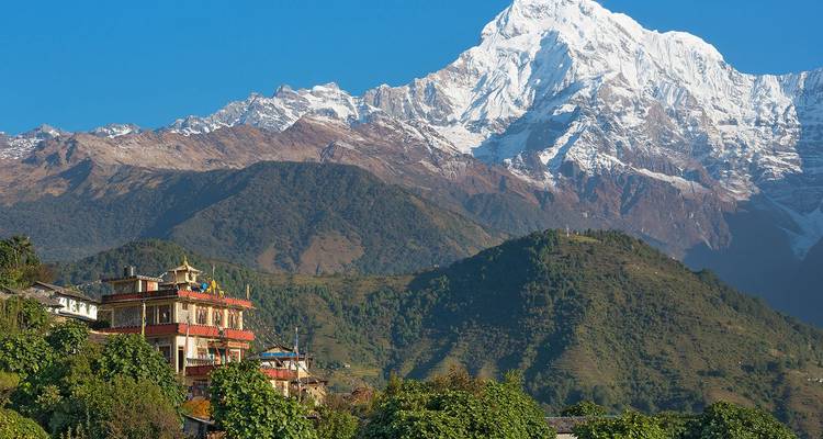 Hillside monastery and clustered village sit beneath towering white Himalayan peaks and green forested slopes.