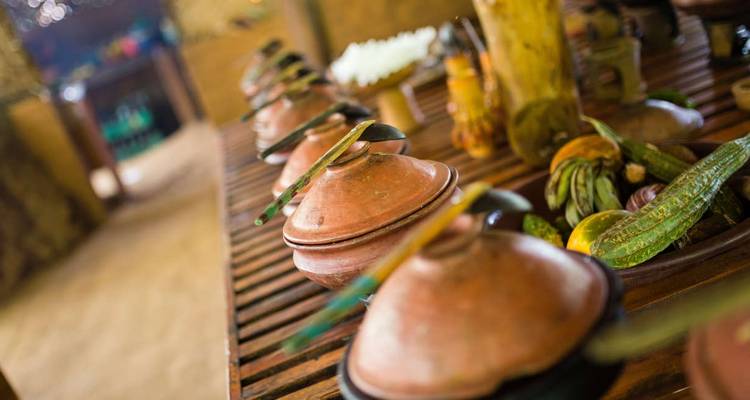 Rangée de pots en terre cuite traditionnels avec des cuillères en bois posés sur une table rustique prête pour un repas.