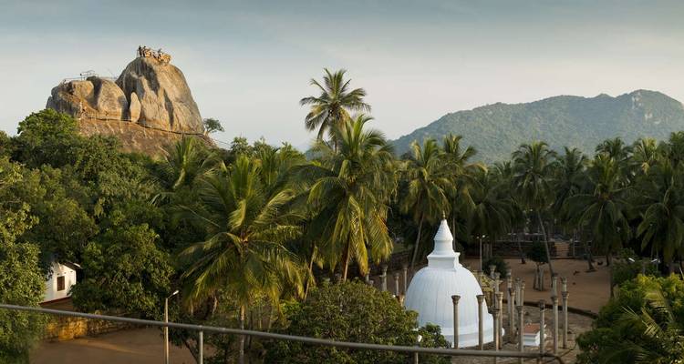 Stupa blanc niché parmi les palmiers avec un point de vue rocheux au-dessus à Mihintale.