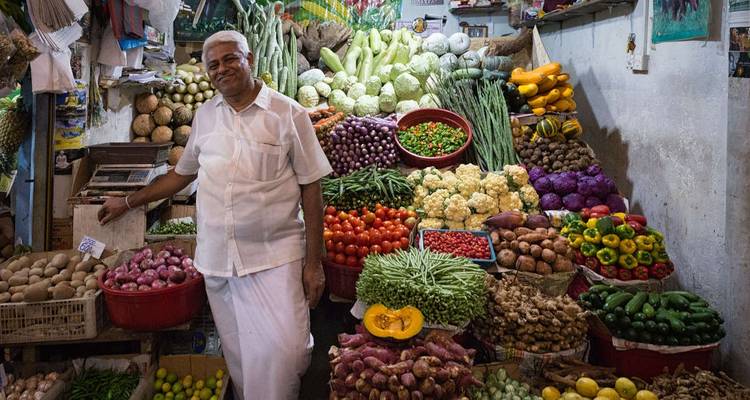 Un vendeur du marché sourit à côté d'un étalage vibrant de légumes et de fruits frais.