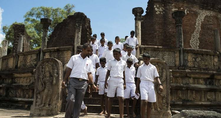Group of school children and a teacher walking through ruins.