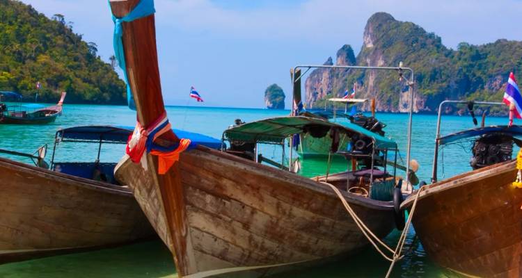 Traditionele longtailboten deinen op turkooizen water tegen kalkstenen rotsen en jungle op Thailands Phi Phi eilanden.