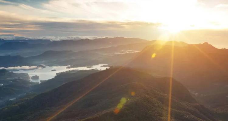 Sonnenstrahlen werfen goldenes Licht über neblige Seen und sanfte Berghänge in der Nähe des Adam's Peak in Sri Lanka.
