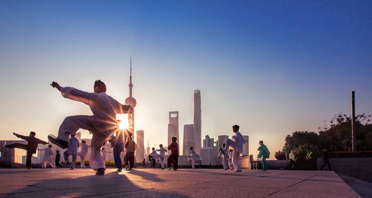 Personas practicando Tai Chi con el horizonte de una ciudad de fondo.