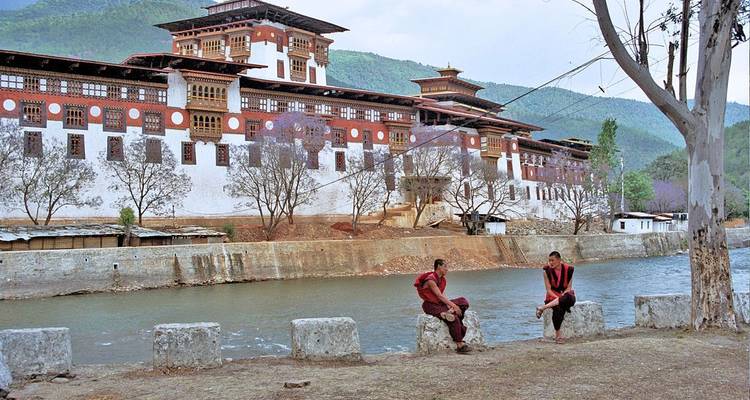 Monjes conversando junto a un edificio tradicional butanés al lado de un río.