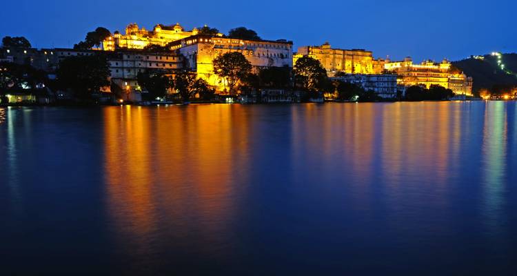 Night view of a sprawling palace illuminated by lights by a lake.