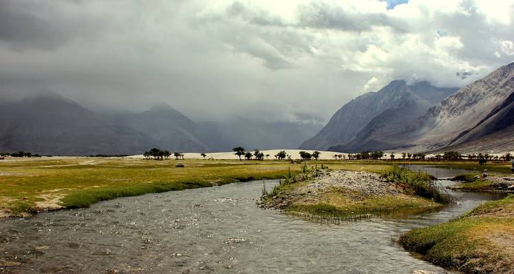 Mountain landscape with clouds and a flowing stream.