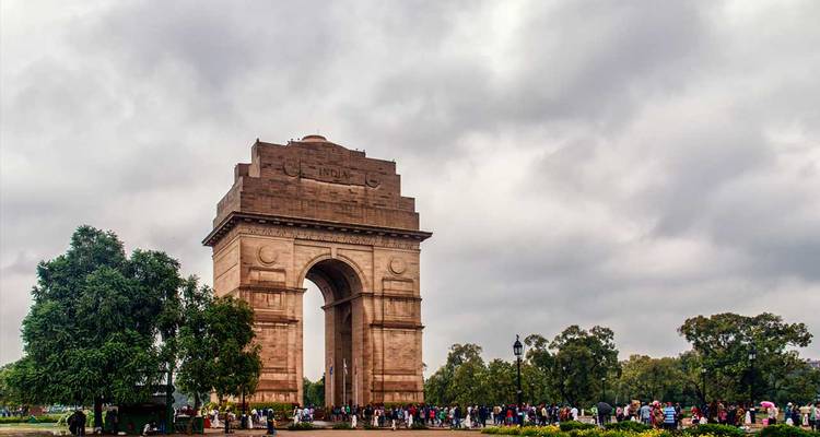 India Gate torens uit boven een menigte bezoekers onder een grijze bewolkte hemel in het centrum van New Delhi.