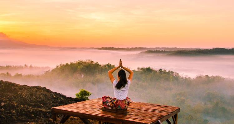 Personne pratiquant le yoga sur une plateforme avec une vue magnifique sur le lever du soleil.