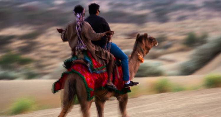 Zwei Menschen reiten auf einem Kamel in der Wüste.