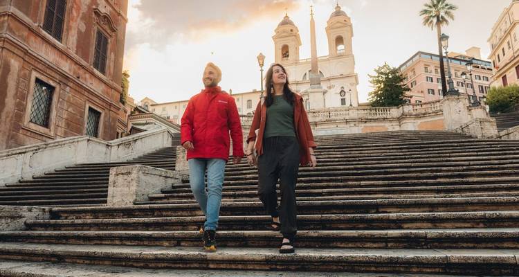 Un couple descend les marches historiques de la Trinité-des-Monts à l'aube avec l'horizon de Rome qui brille derrière.