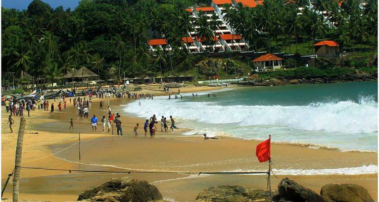 Multitudes disfrutando de una playa con olas grandes y un resort en el fondo.