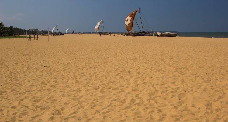 Wide sandy beach with traditional boats and people walking.
