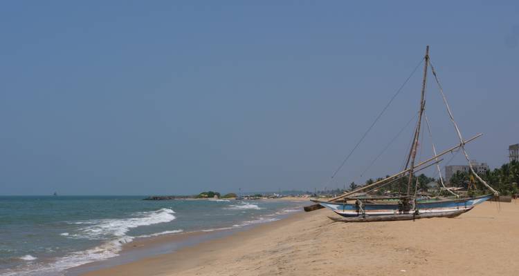 Sailboat on a sandy beach with ocean waves and clear sky.