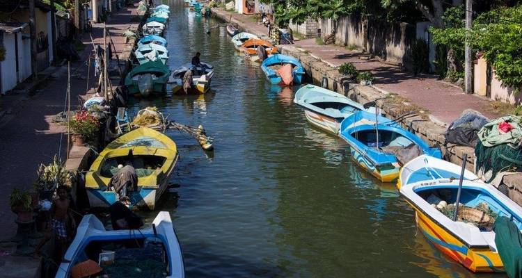 Colorful boats lined up in a narrow canal in a bustling area.