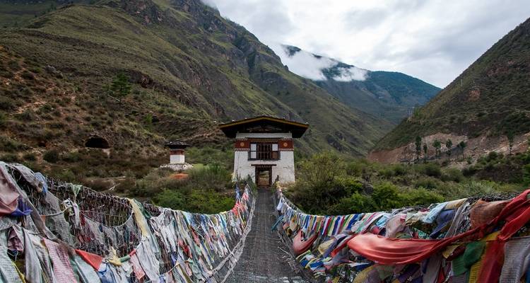 Puente colgante con banderas de oración y vistas a la montaña.